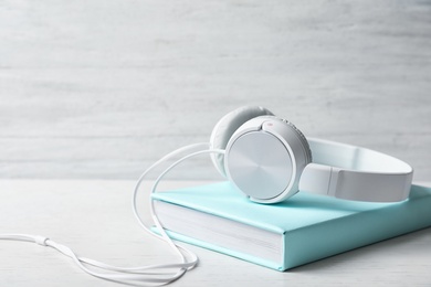 Photo of Modern headphones with hardcover book on wooden table. Space for text