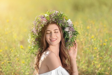 Photo of Young woman wearing wreath made of beautiful flowers in field on sunny day