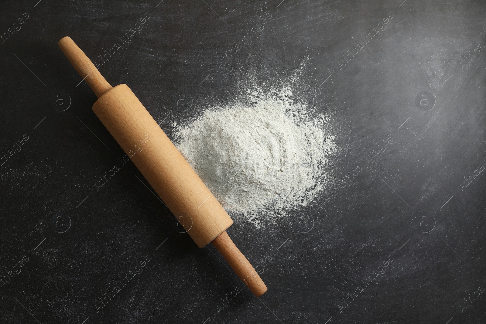 Photo of Flour and rolling pin on black table, top view