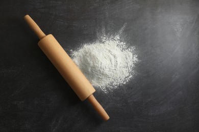 Flour and rolling pin on black table, top view