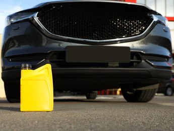 Photo of Yellow canister with motor oil near car on asphalt road, low angle view