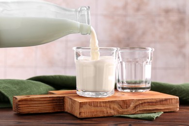 Photo of Pouring milk from bottle into glass at wooden table, closeup