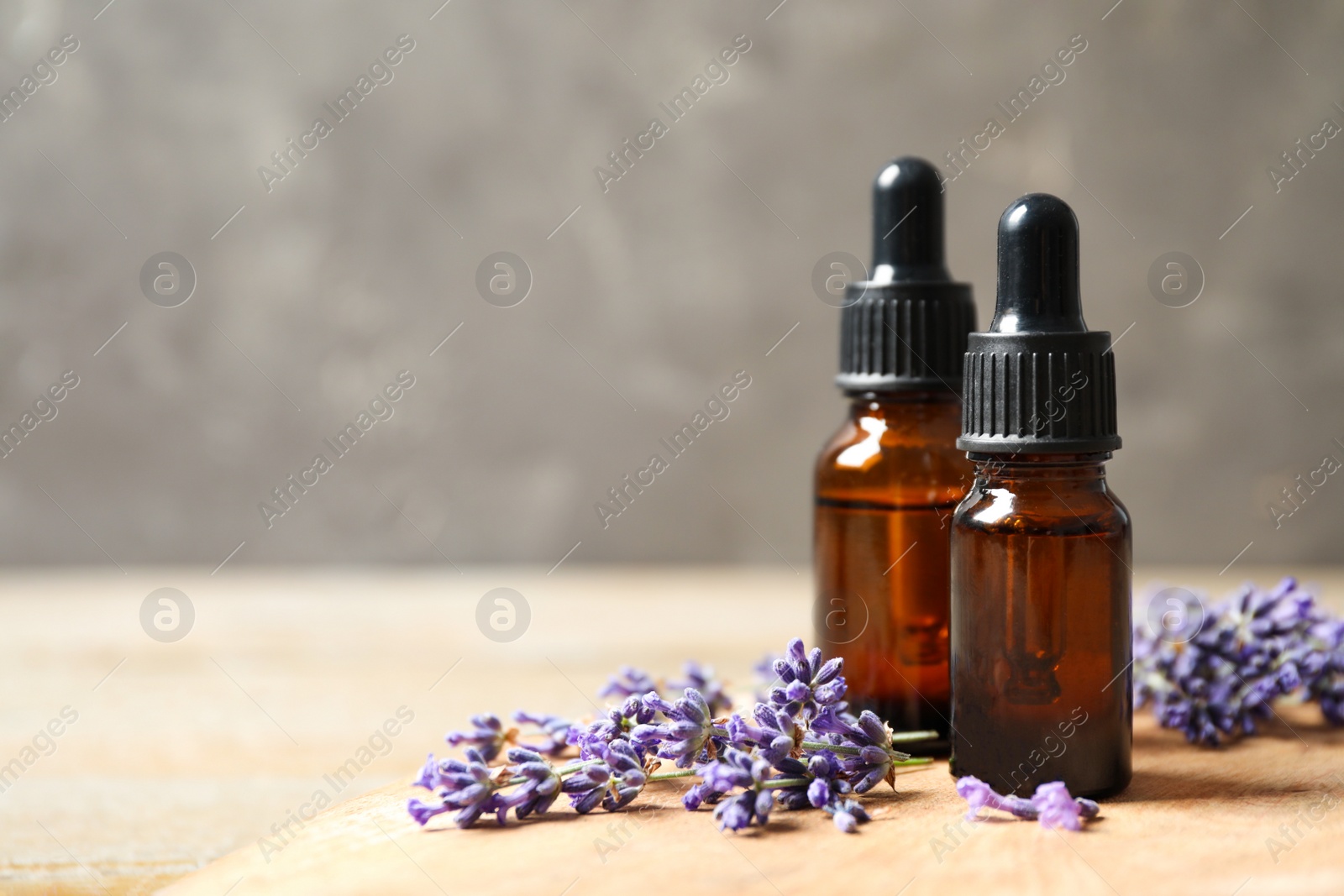 Photo of Bottles of essential oil and lavender flowers on wooden table. Space for text