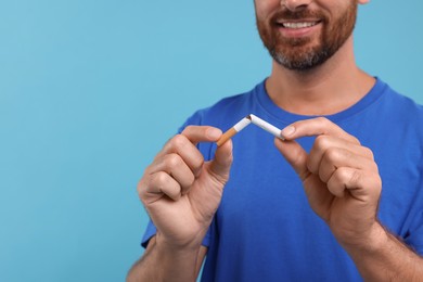 Photo of Stop smoking concept. Man breaking cigarette on light blue background, closeup. Space for text