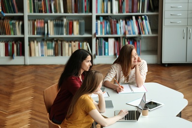 Photo of Young women discussing group project at table in library