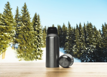 Image of Thermos bottle on wooden table in snowy forest