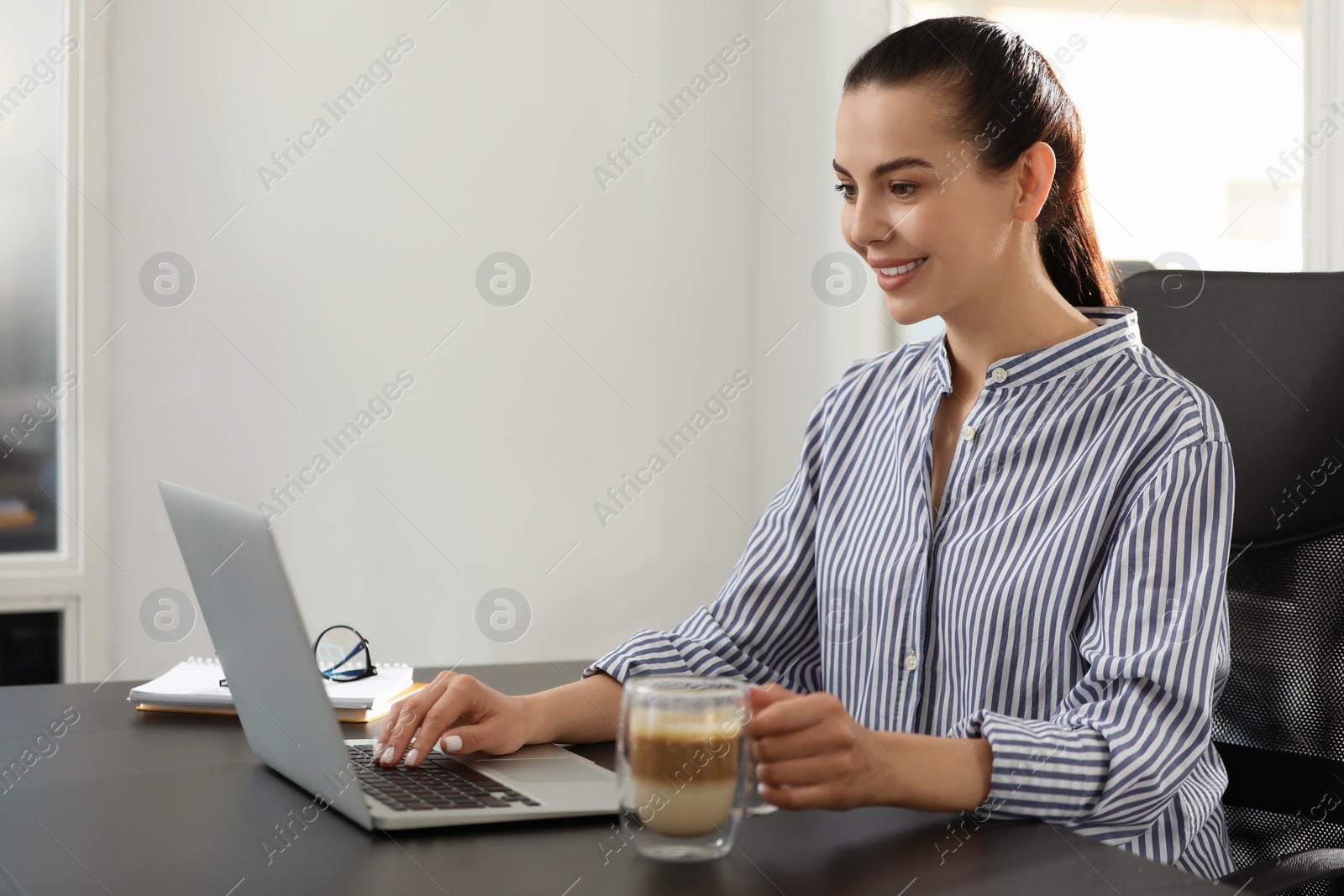 Photo of Happy woman using modern laptop at black desk in office