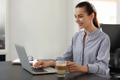 Happy woman using modern laptop at black desk in office