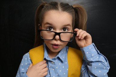 Photo of Cute child wearing glasses near chalkboard, closeup. First time at school
