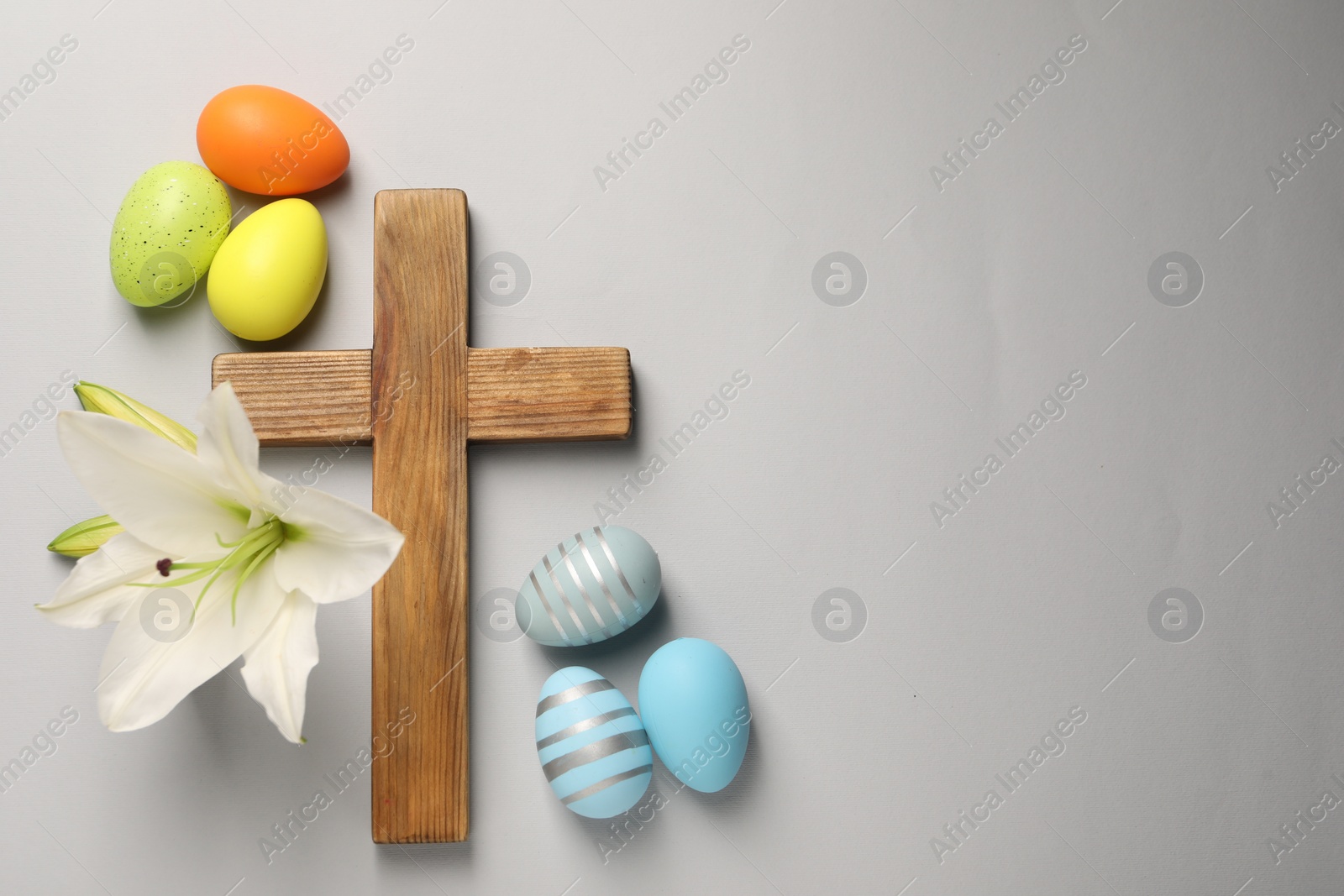 Photo of Wooden cross, painted Easter eggs and lily flowers on grey background, flat lay. Space for text