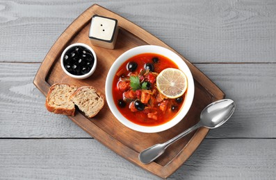 Photo of Meat solyanka soup with sausages, olives and vegetables in bowl served on grey wooden table, top view