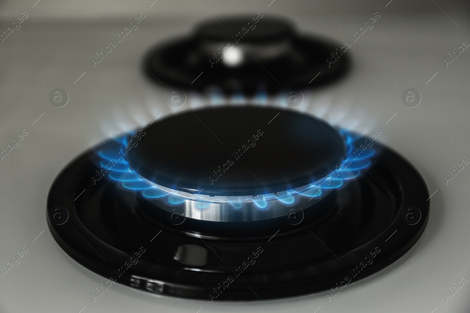 Photo of Gas burner with blue flame on modern stove, closeup