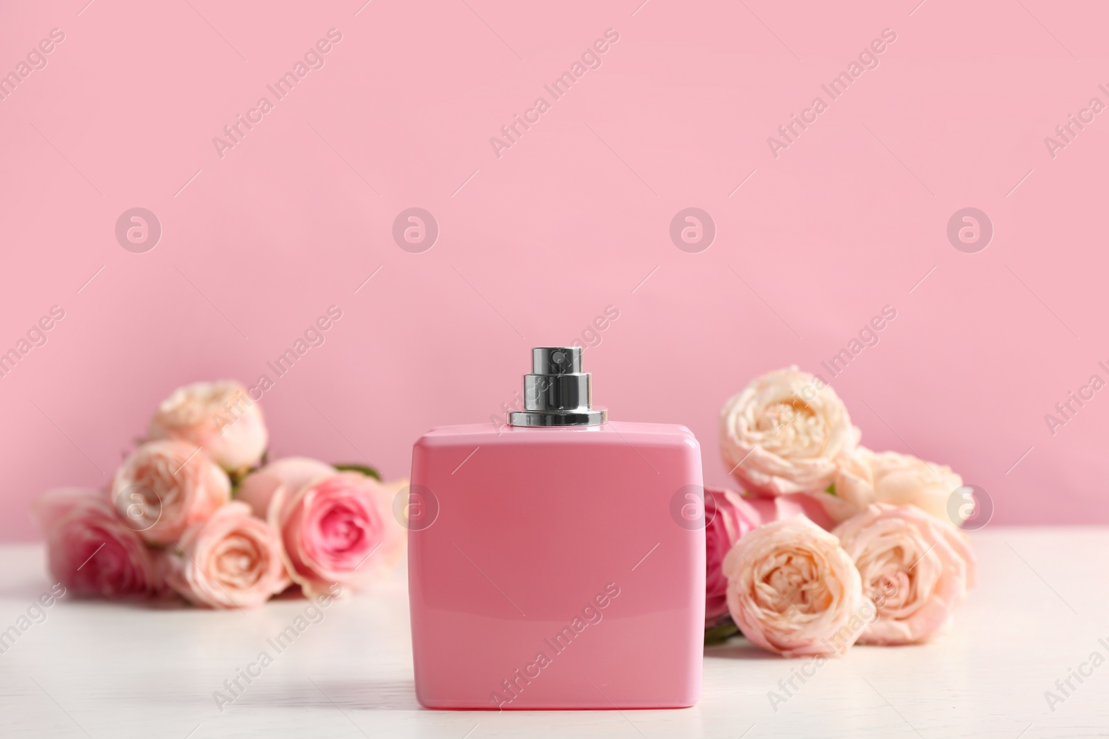Photo of Bottle of perfume with beautiful roses on table