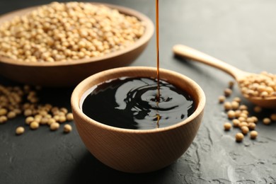 Photo of Pouring tasty soy sauce into bowl on black table, closeup