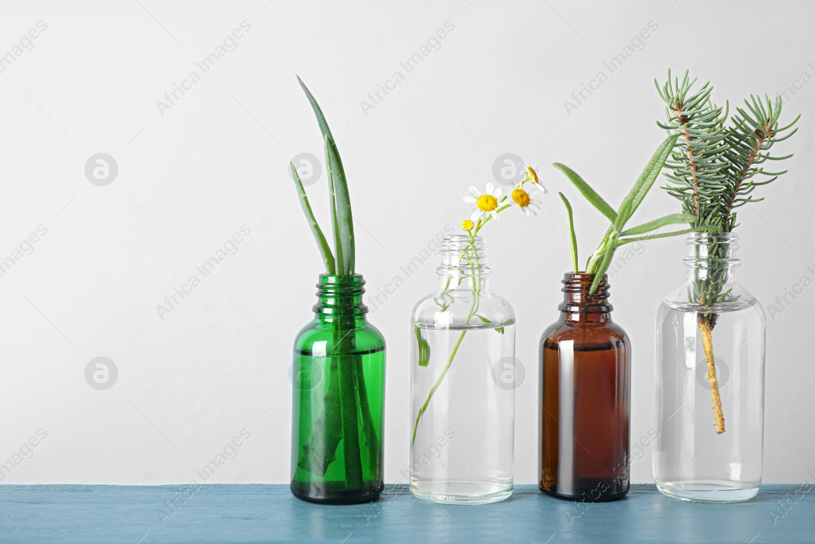 Photo of Glass bottles of different essential oils with plants on table. Space for text