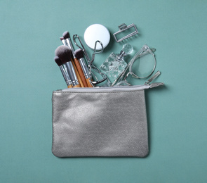 Photo of Cosmetic bag with makeup products and beauty accessories on blue-gray background, flat lay