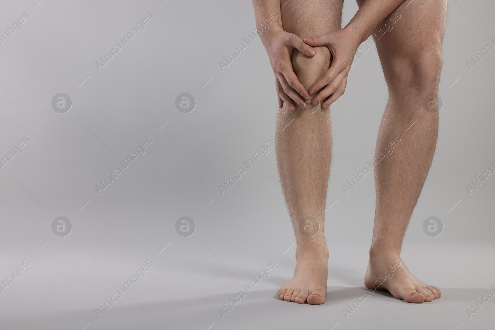 Photo of Man suffering from leg pain on grey background, closeup. Space for text