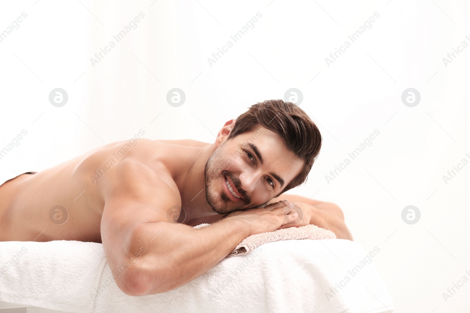 Photo of Handsome young man relaxing on massage table against light background, space for text. Spa salon