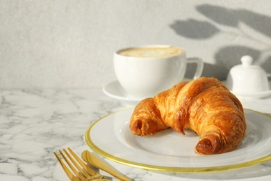 Delicious fresh croissant served with coffee on white marble table, closeup. Space for text