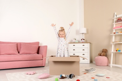 Photo of Cute little girl playing with cardboard box at home