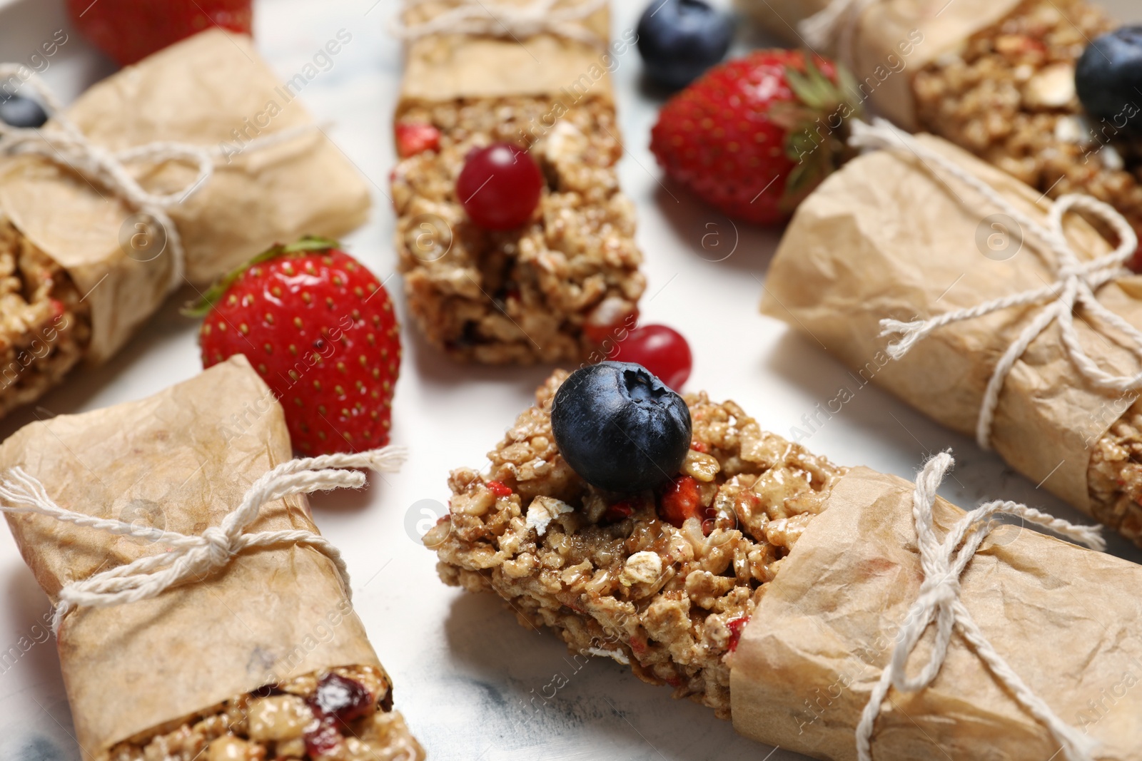 Photo of Tasty granola bars and berries on white table, closeup