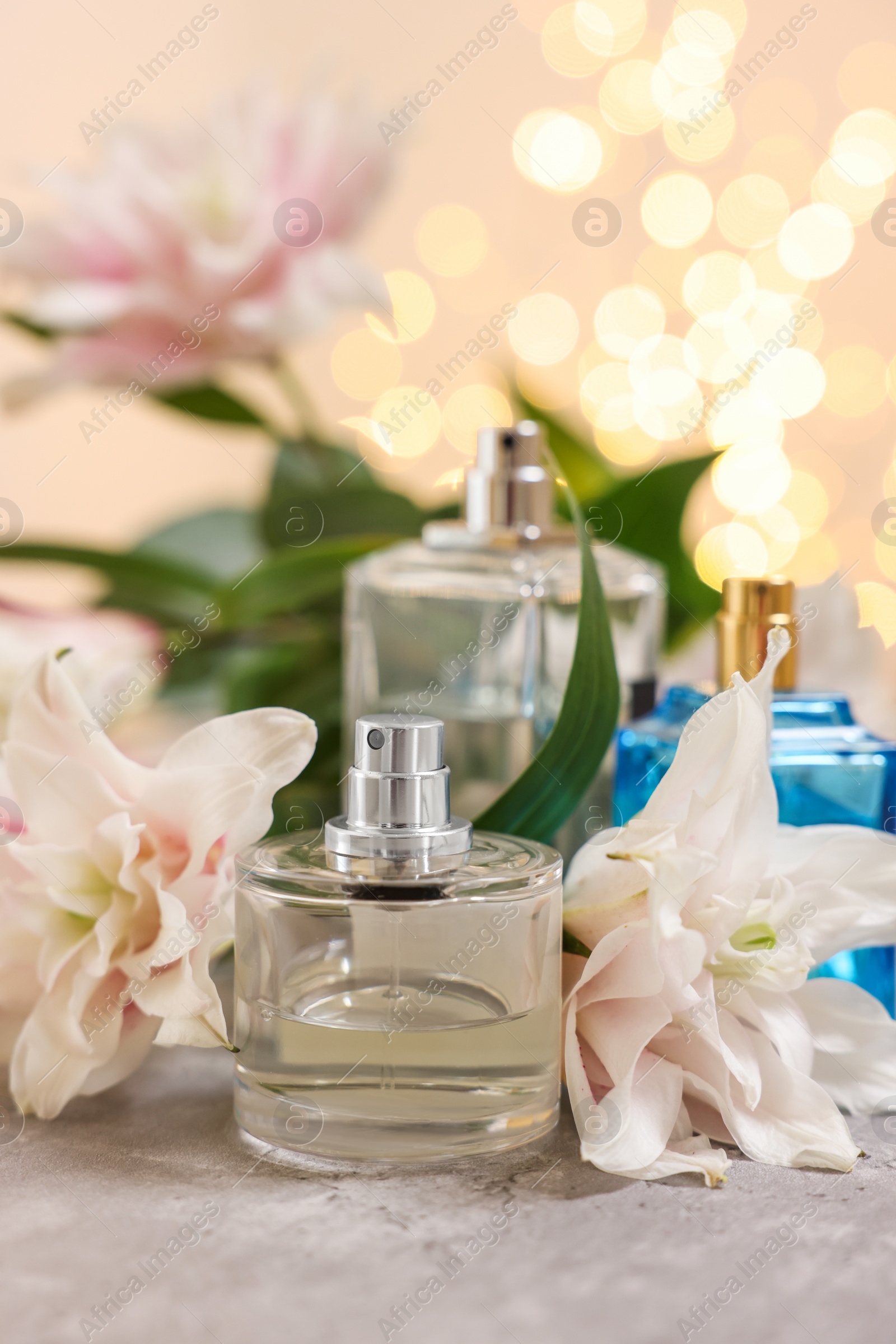 Photo of Bottlesperfume and beautiful lily flowers on table against beige background with blurred lights, closeup