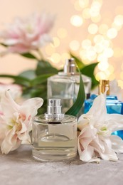 Bottles of perfume and beautiful lily flowers on table against beige background with blurred lights, closeup