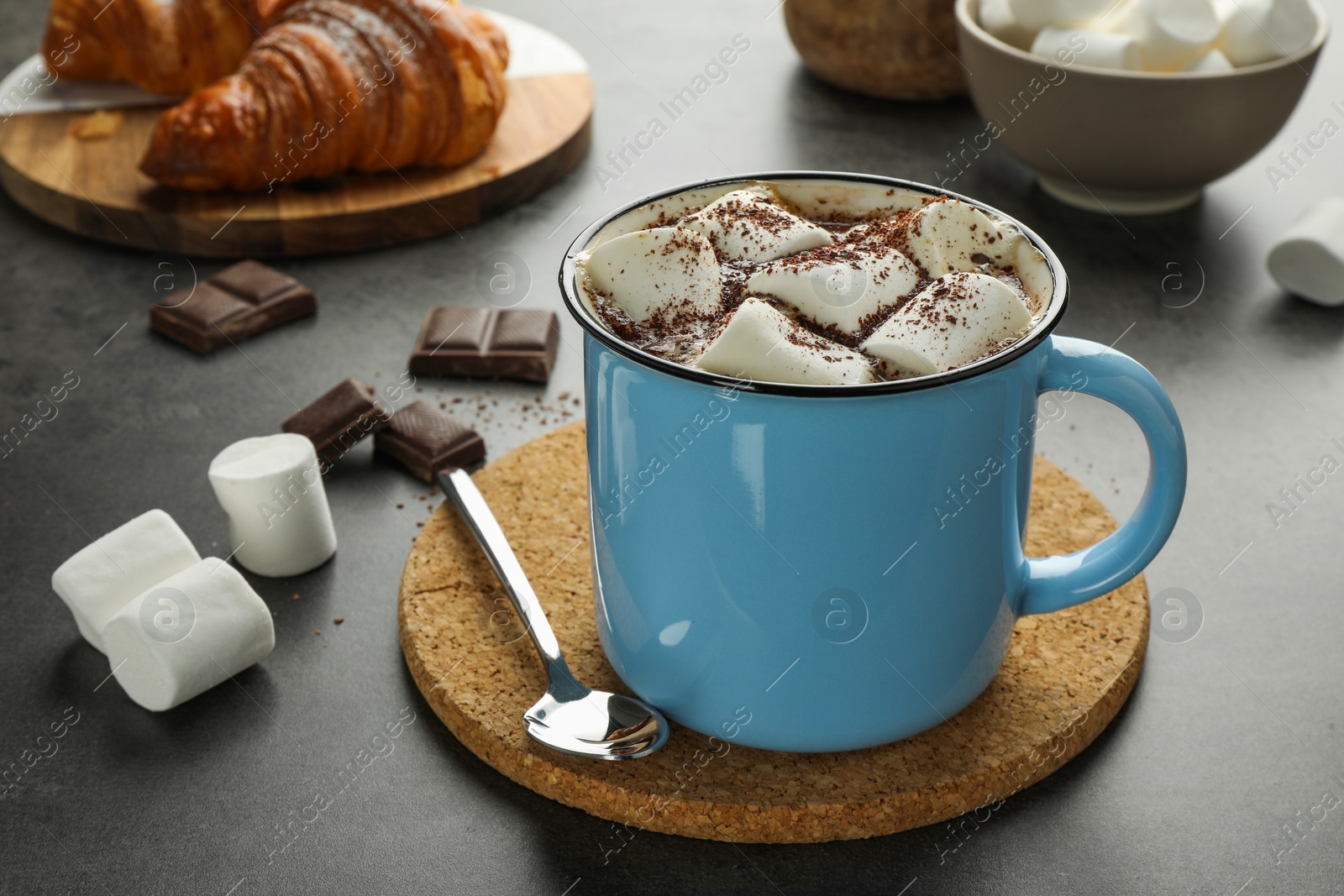 Photo of Delicious hot chocolate with marshmallows, cocoa powder and spoon on grey table, closeup