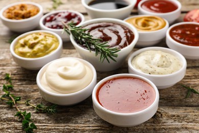Different tasty sauces in bowls, rosemary and thyme on wooden table, closeup
