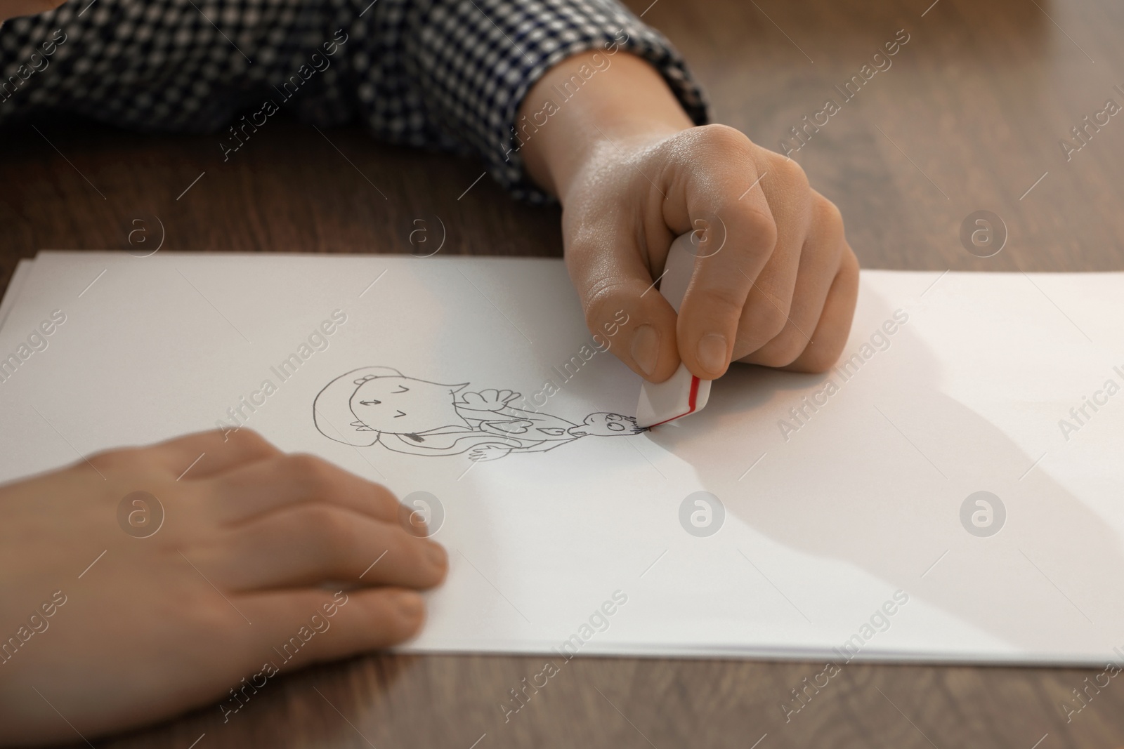 Photo of Boy erasing mistake in his notebook at wooden desk, closeup