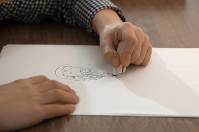 Boy erasing mistake in his notebook at wooden desk, closeup