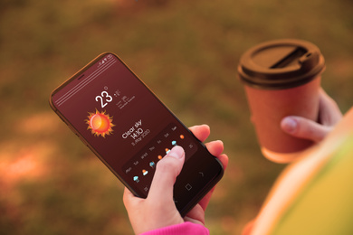 Woman using weather forecast app on smartphone outdoors, closeup