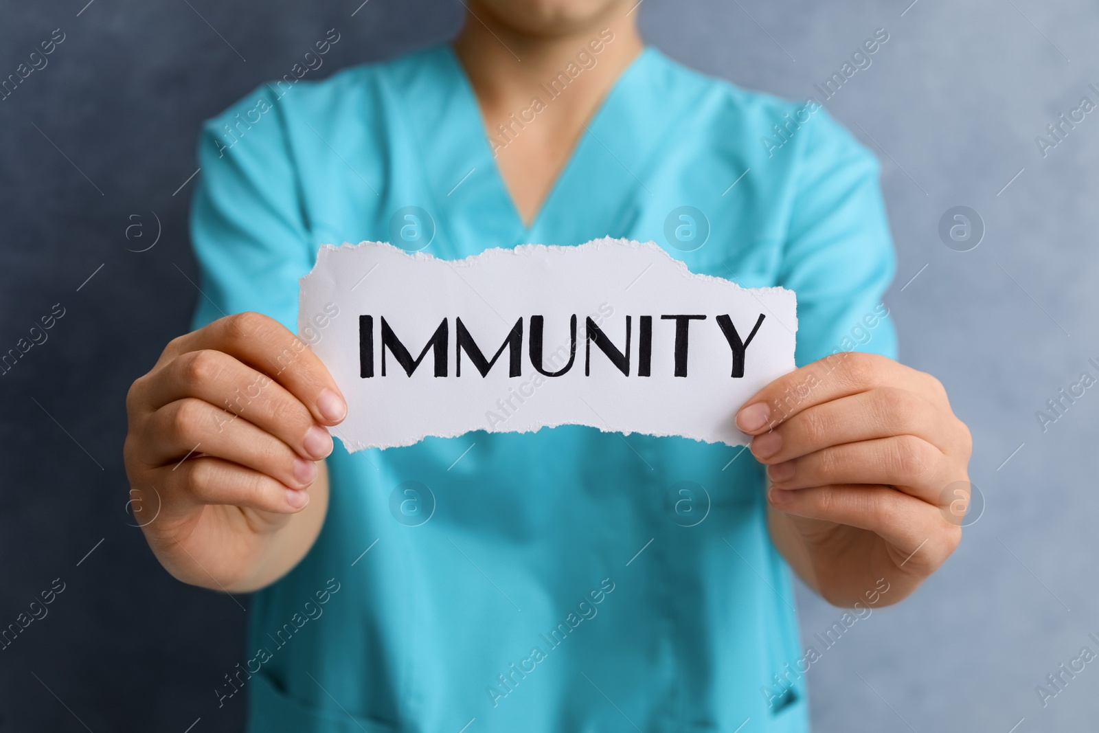 Photo of Woman holding paper piece with word Immunity on blue background, closeup