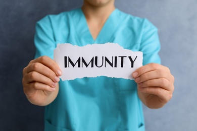 Woman holding paper piece with word Immunity on blue background, closeup