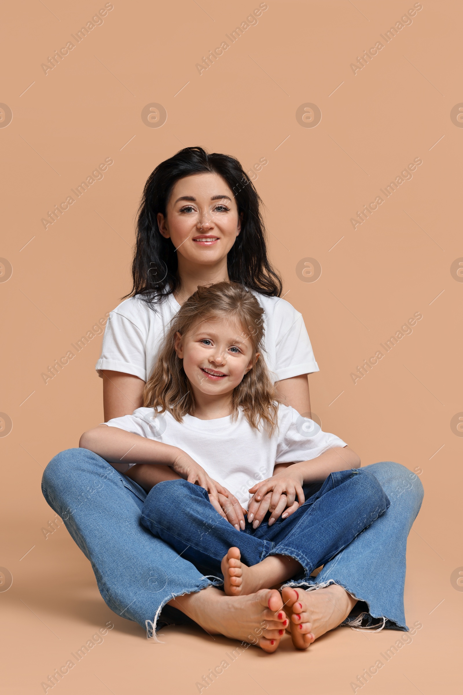 Photo of Beautiful mother with little daughter sitting on beige background