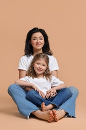 Beautiful mother with little daughter sitting on beige background