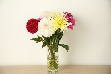 Bouquet of beautiful Dahlia flowers in vase on wooden table near white wall