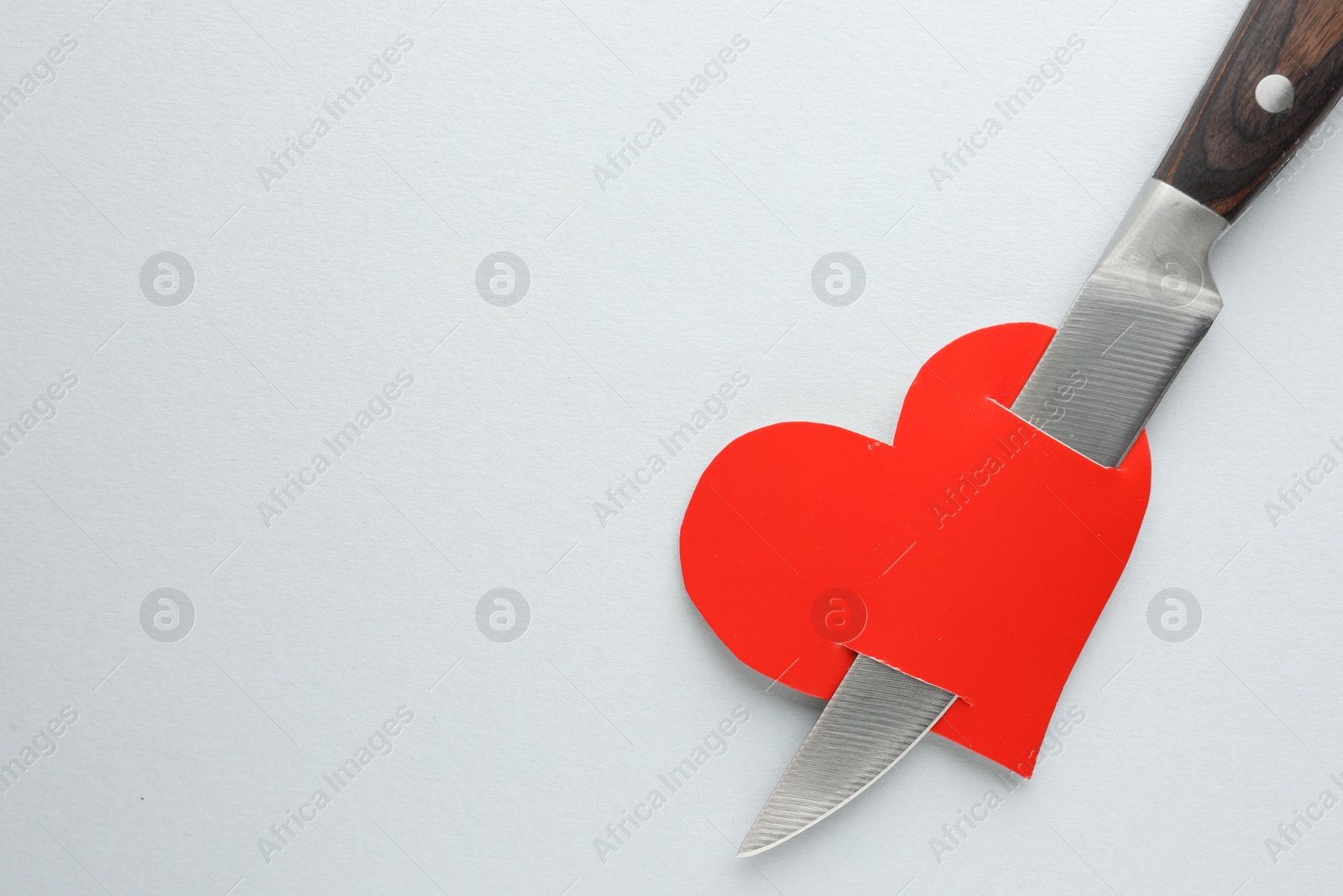 Photo of Broken heart. Red paper heart pierced with knife on white background, top view. Space for text