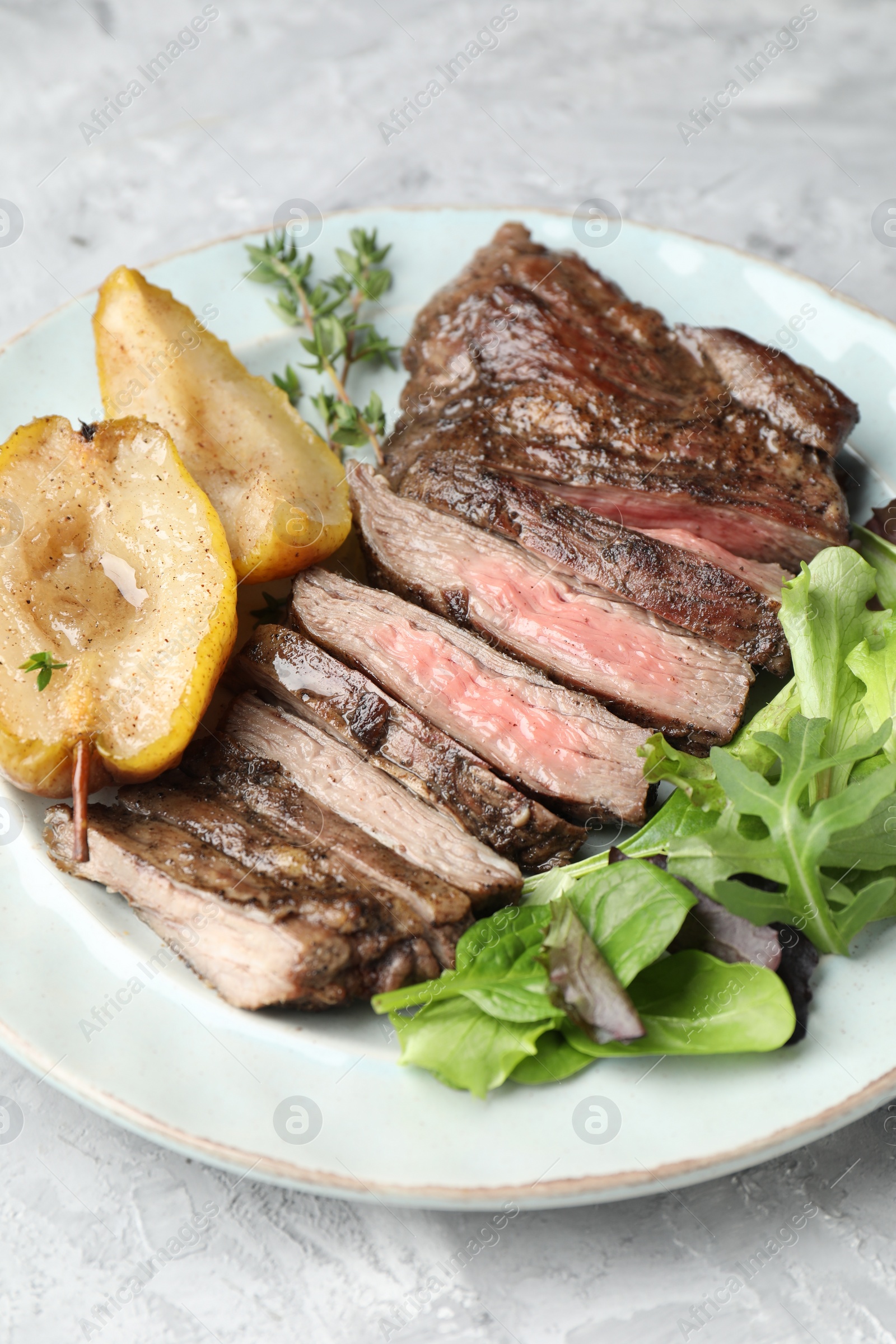 Photo of Pieces of delicious roasted beef meat, caramelized pear and greens on light textured table, closeup