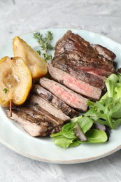 Photo of Pieces of delicious roasted beef meat, caramelized pear and greens on light textured table, closeup