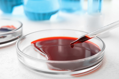 Image of Dripping blood from pipette into Petri dish on table, closeup. Laboratory analysis