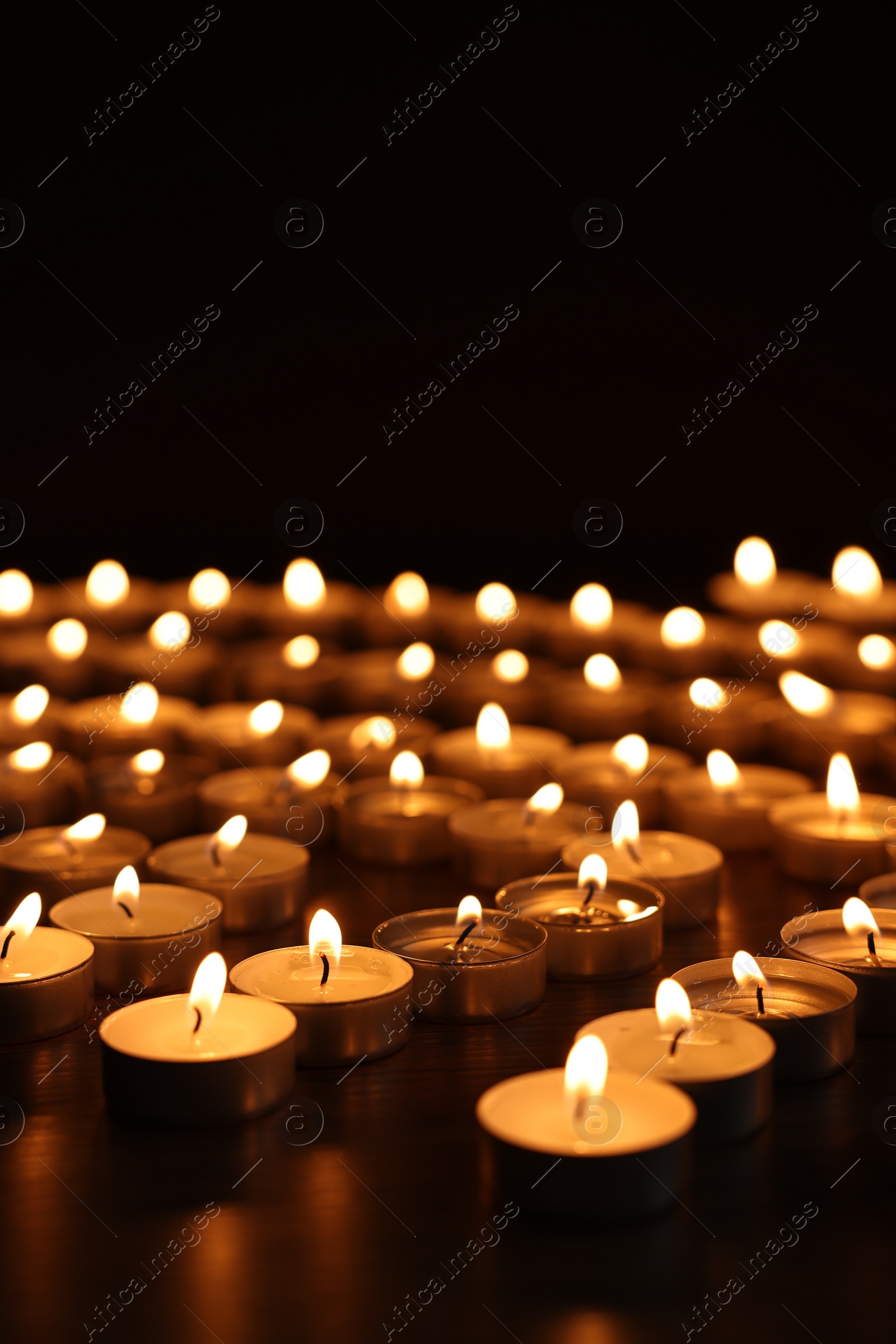 Photo of Burning candles on dark surface against black background