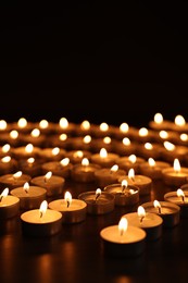 Burning candles on dark surface against black background