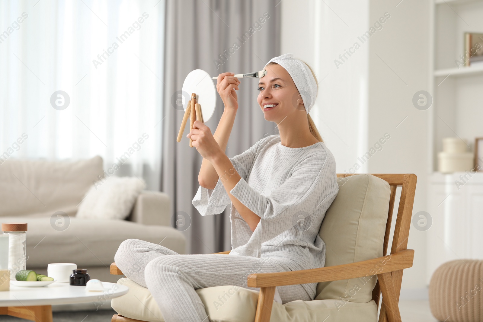 Photo of Young woman applying face mask in front of mirror at home. Spa treatments