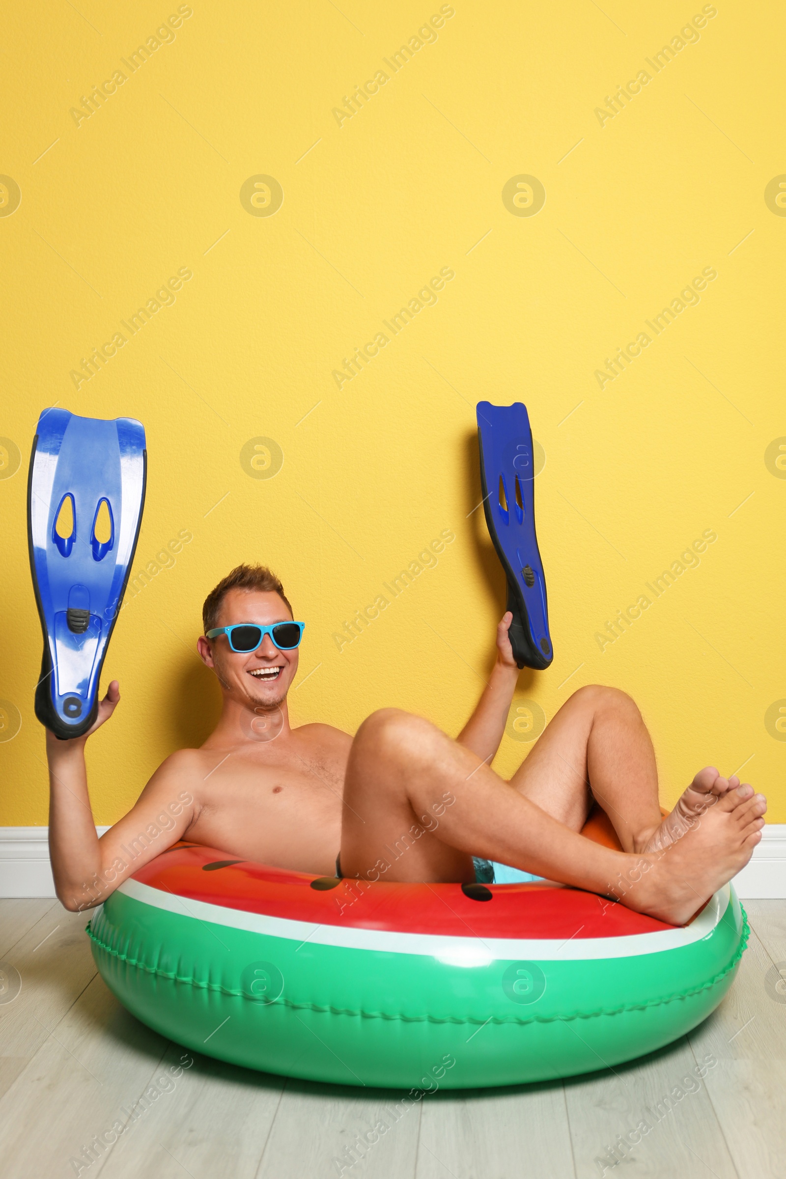 Photo of Shirtless man with inflatable ring and flippers having fun on floor near color wall