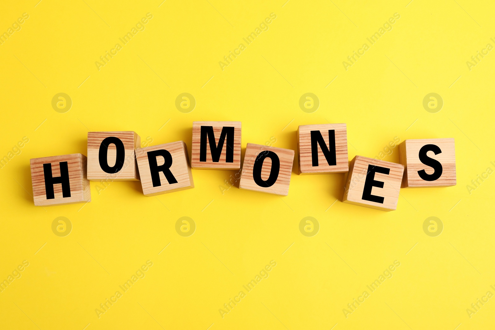 Photo of Word Hormones made of wooden cubes with letters on yellow background, flat lay