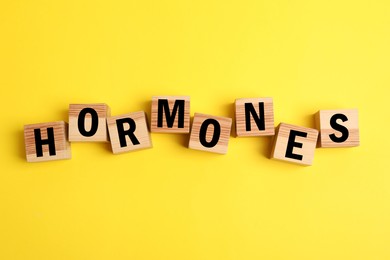 Photo of Word Hormones made of wooden cubes with letters on yellow background, flat lay
