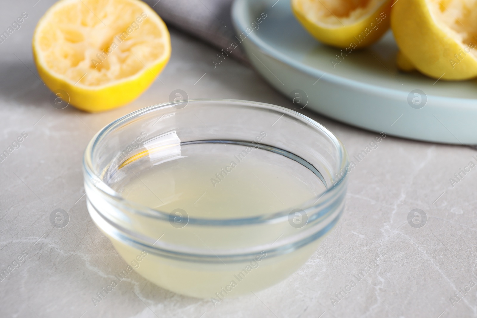 Photo of Freshly squeezed lemon juice in glass bowl on grey marble table