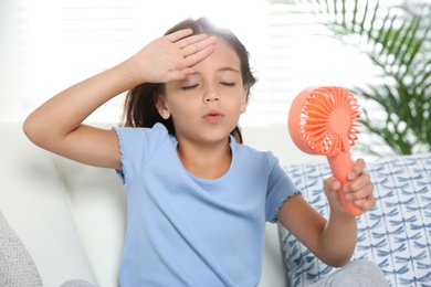 Photo of Little girl with portable fan suffering from heat at home. Summer season