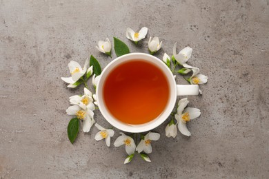 Cup of aromatic jasmine tea and fresh flowers on grey table, flat lay